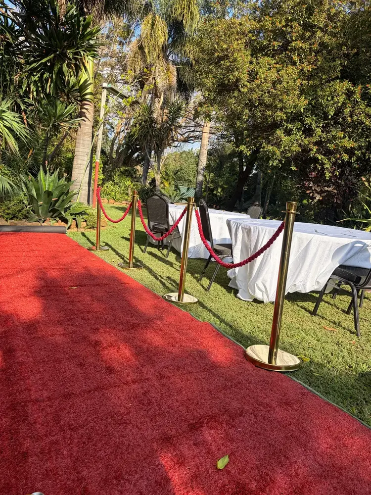 Red carpet, gold stanchions, tables and chairs arranged for an outdoor event